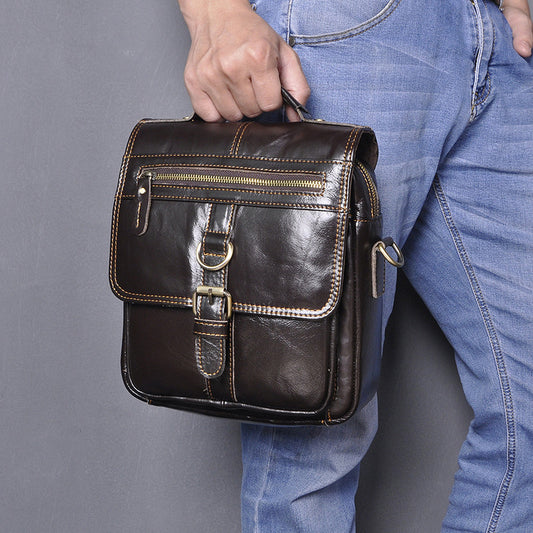 Man holding compact men's crossbody leather bag in coffee color with buckle and zipper detail