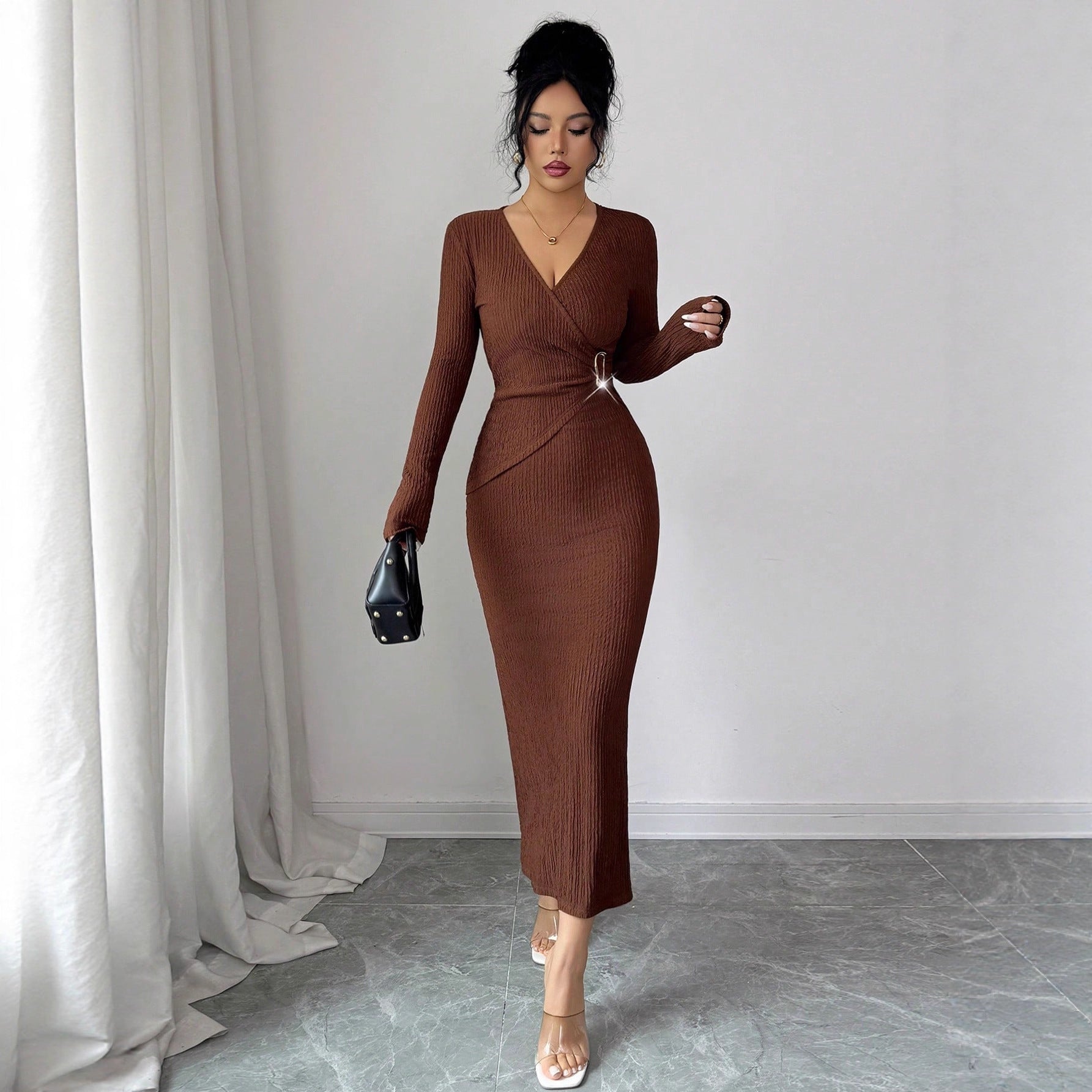 Woman wearing a slim-fit coffee brown knit dress with long sleeves holding a black handbag