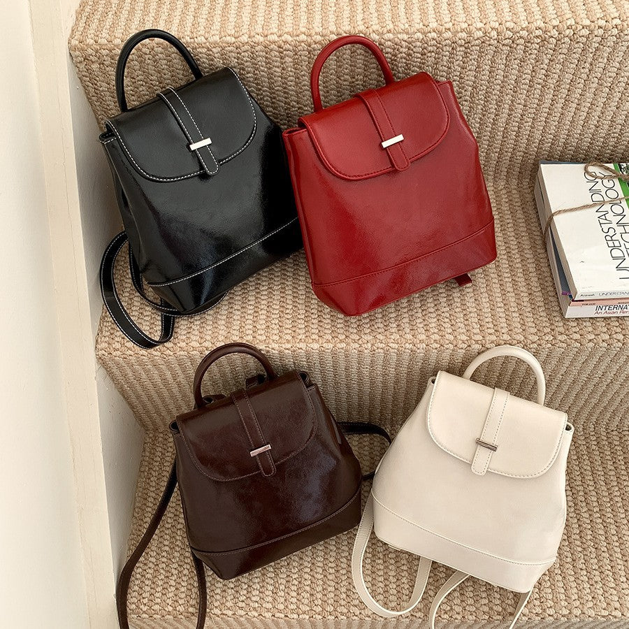Four PU leather small backpacks in black, red, brown, and beige on beige carpeted stairs with stacked books
