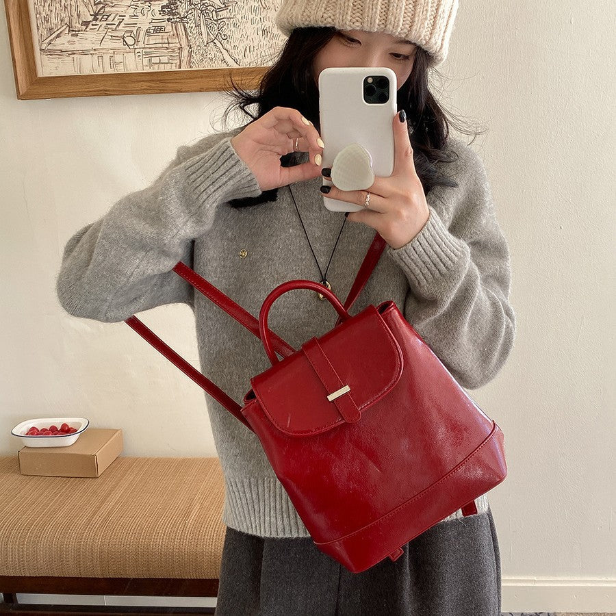 Woman wearing beige knit hat and grey sweater holding red PU leather backpack in neutral room