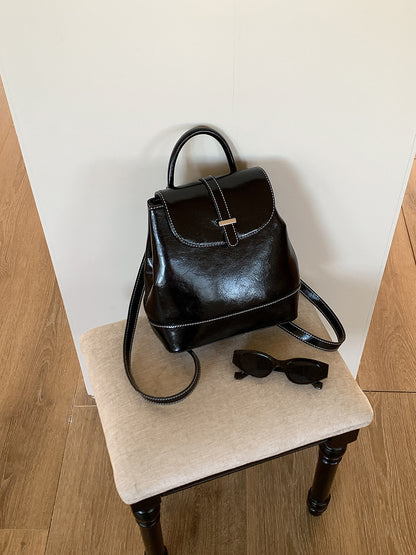 Black PU leather small backpack on beige cushioned chair with black sunglasses beside it