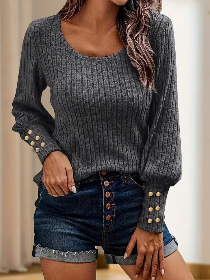 Woman wearing dark gray ribbed long sleeve sweater with gold button details on cuffs and high-waisted denim shorts