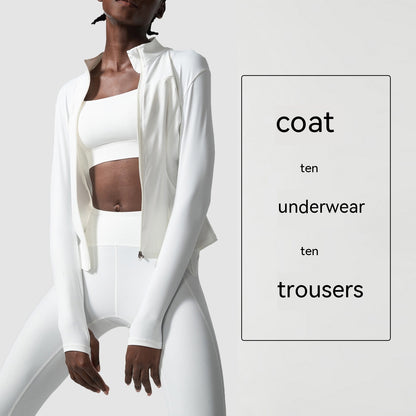 woman wearing all-white activewear set including coat, sports bra, and high-waisted leggings in minimal studio