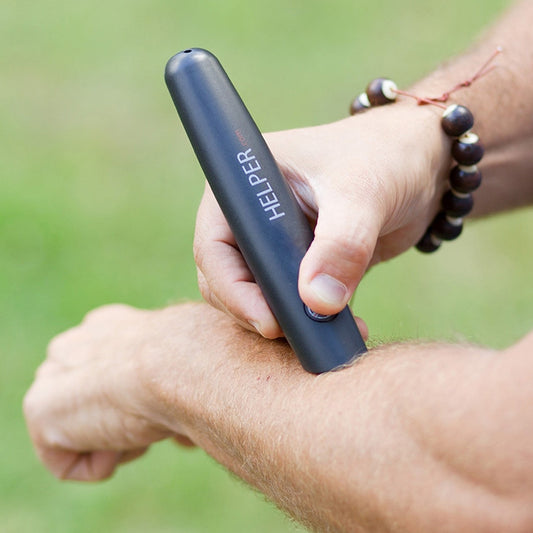 Person using black Helper Mosquito Bite Relief device on arm outdoors with green background