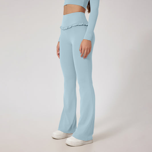 Woman wearing light blue high-waist yoga pants and matching crop top with ruffle detail, standing on white background
