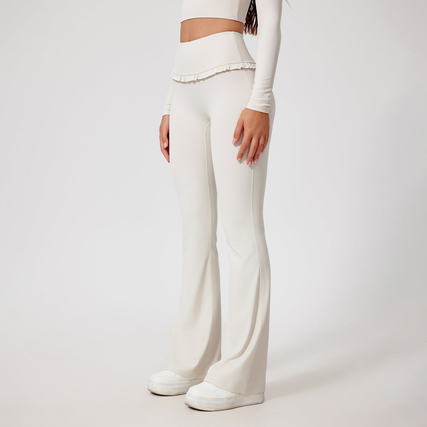 Woman wearing white high-waist yoga pants with ruffle detail and white sneakers