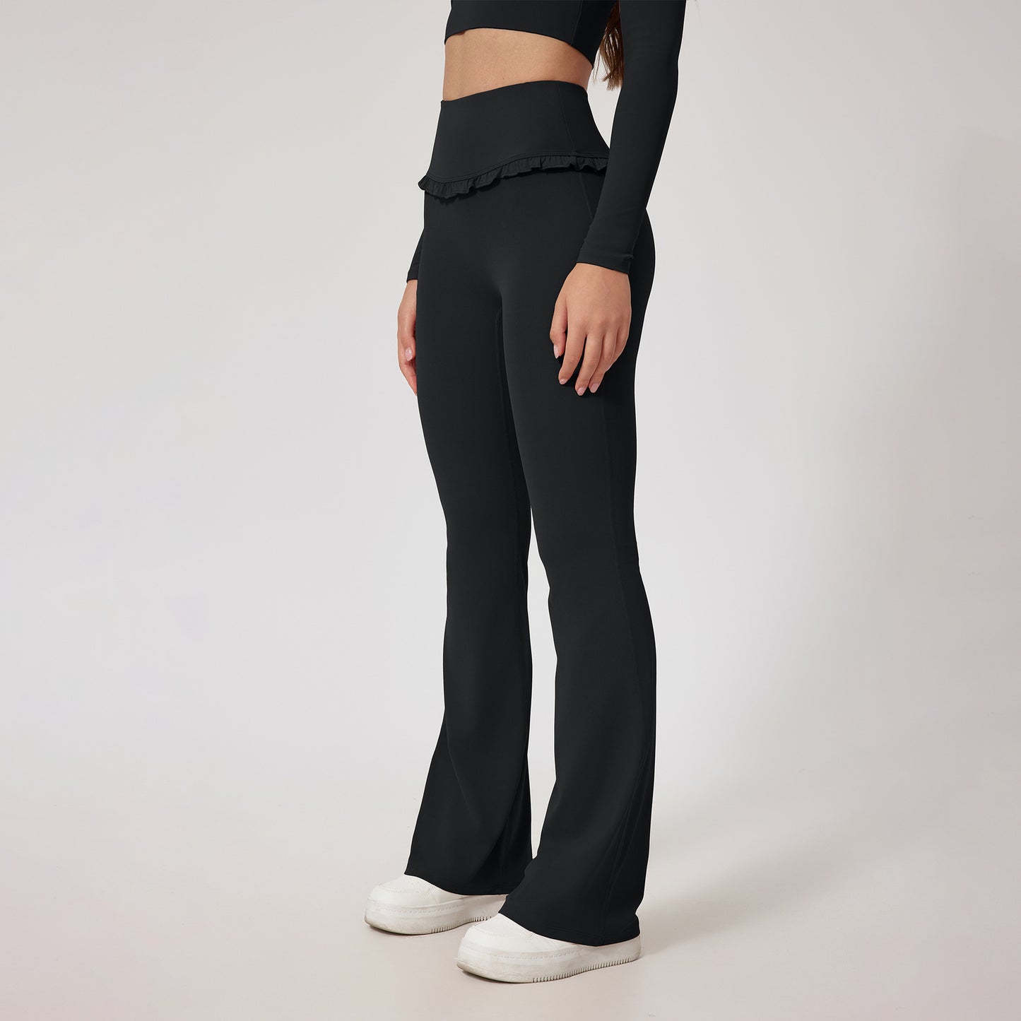 Woman wearing black high-waist flared yoga pants with ruffle detail and white sneakers