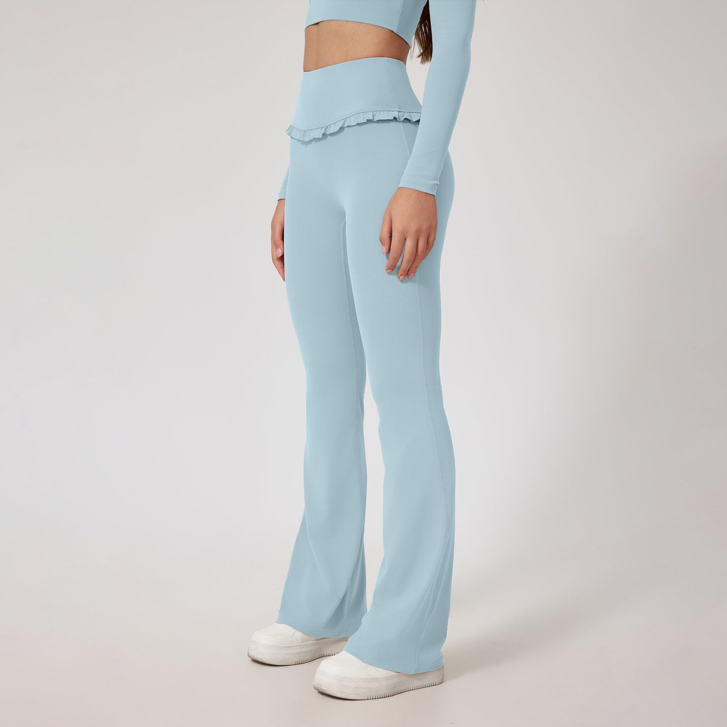 woman wearing light blue high waist flare yoga pants with ruffle detail and matching crop top