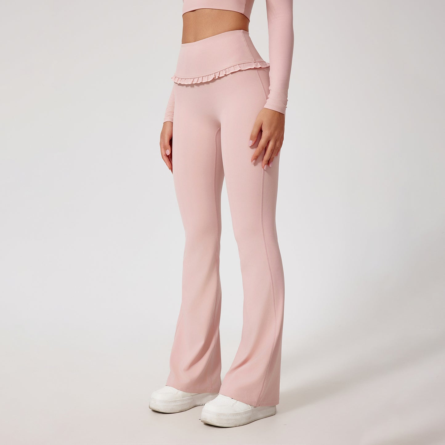 Woman wearing pale pink high-waist flared yoga pants with ruffled waistband and white sneakers