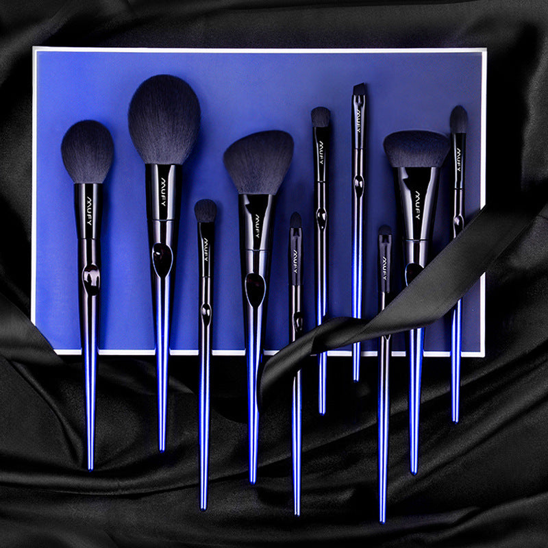 Set of 10 blue nylon bristle makeup brushes with black handles on blue box, displayed on black silky fabric