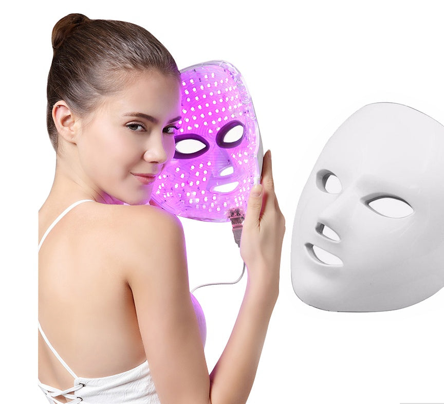 Woman holding purple LED light facial mask with white background and a plain white mask beside
