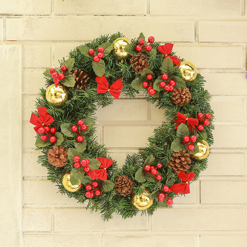 Christmas wreath with green pine branches, red bows, berries, pinecones, and gold ornaments on beige brick wall