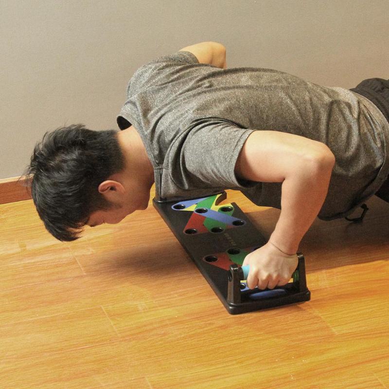 Man performing push-up on a black portable exercise board with multicolor grip positions on wooden floor