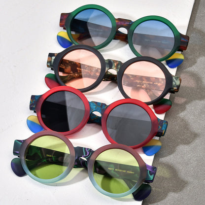 Four pairs of round frosted sunglasses in green, black, red, and purple matte frames with tinted lenses