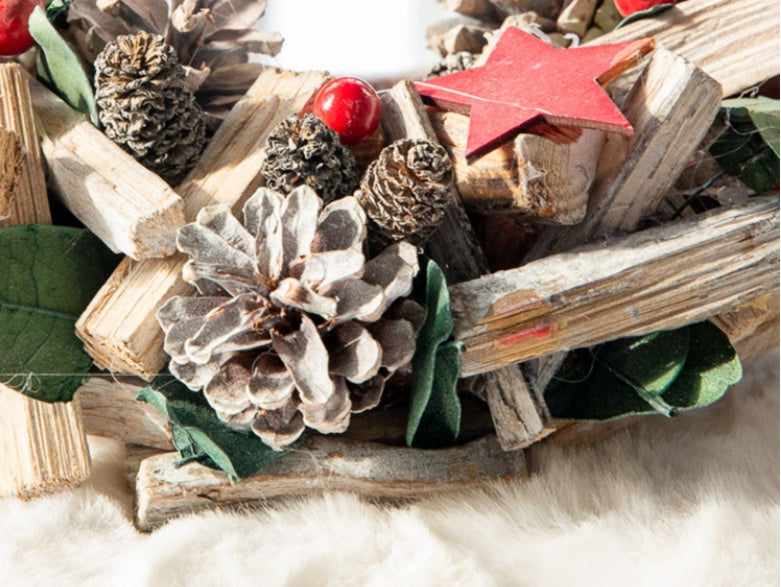 Close-up of a rustic Christmas wreath with pinecones, red berries, green leaves, wooden stars, and twigs on white fur