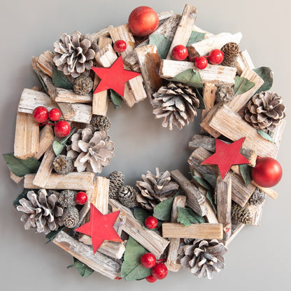 Christmas wreath with rustic wood pieces, pinecones, red stars, red berries, and green leaves