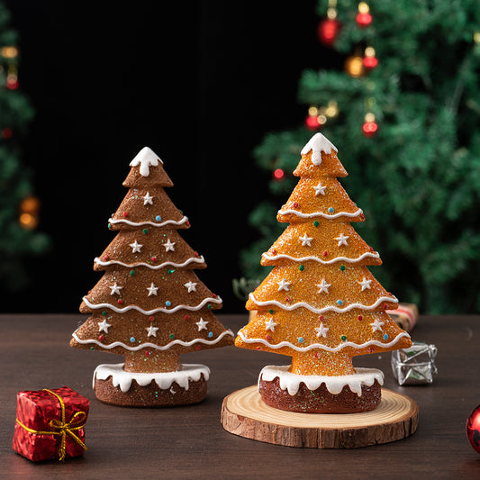 Two festive ginger cake Christmas tree decorations with icing and colorful sprinkles on wooden surface