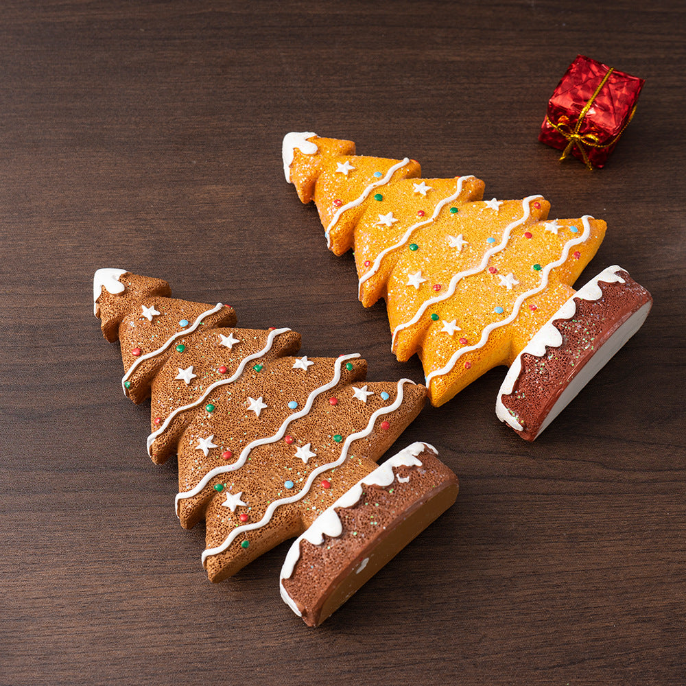 Two decorated ginger cake Christmas tree ornaments with icing and colorful dots on a wooden surface with a small red gift box