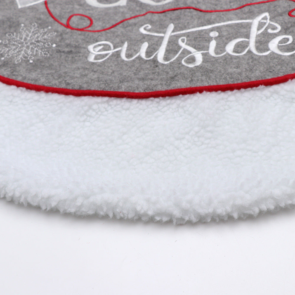 Close-up of gray Christmas tree skirt with white fleece border and red trim featuring snowflake and text design
