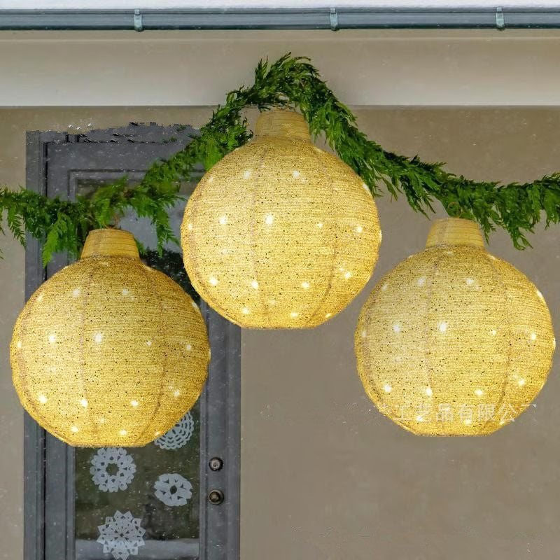 Three glowing round woven lanterns hanging with green garland on a beige wall background