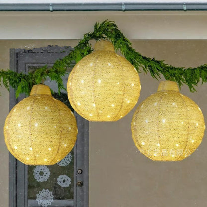 Three glowing round woven lanterns hanging with green garland on a beige wall background