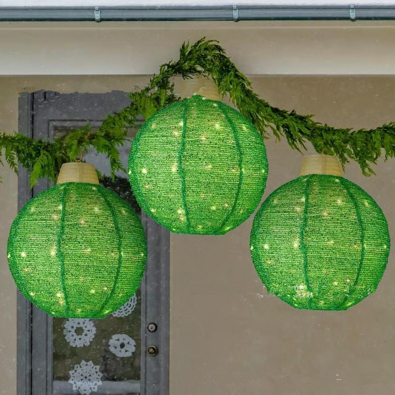 Three glowing green round Christmas lanterns hanging indoors with greenery garland decoration