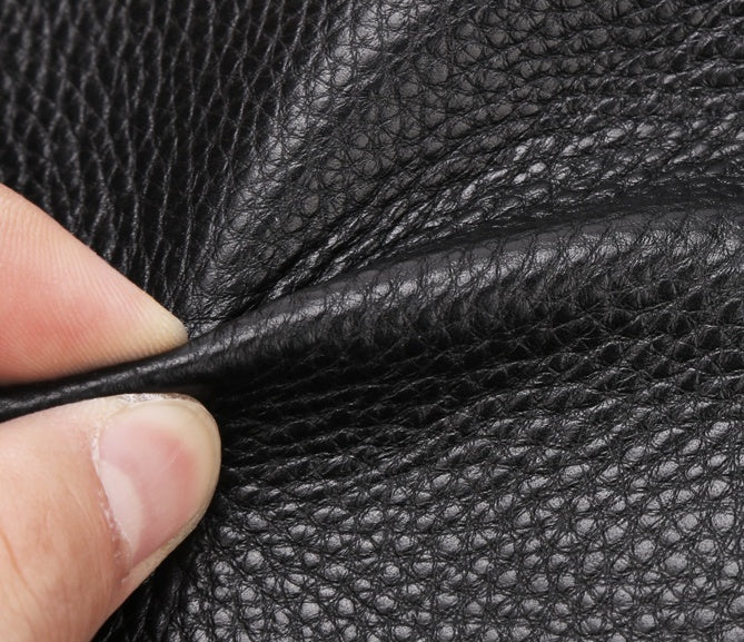 Close-up of hand holding black American bison leather showing textured grain surface