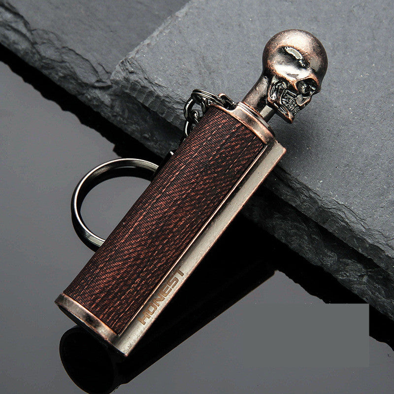 Vintage bronze metal keychain lighter with skull cap and leather texture, placed on slate stone
