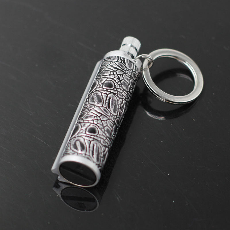 silver metal keychain lighter with textured patterned grip on black surface