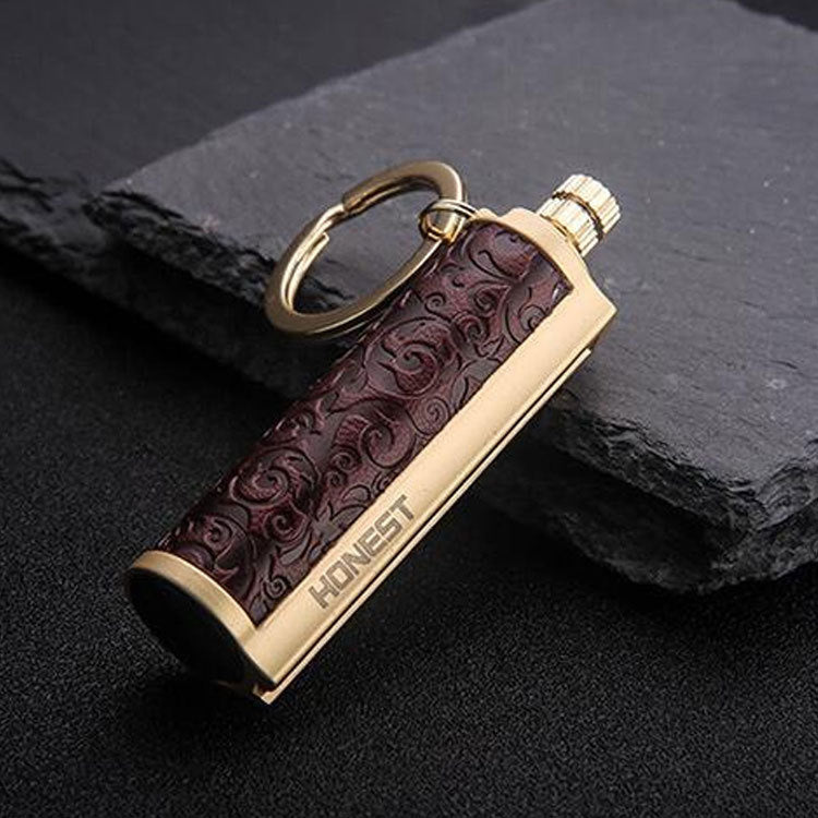 Golden metal keychain lighter with embossed dark brown leather and HONEST engraving on black surface