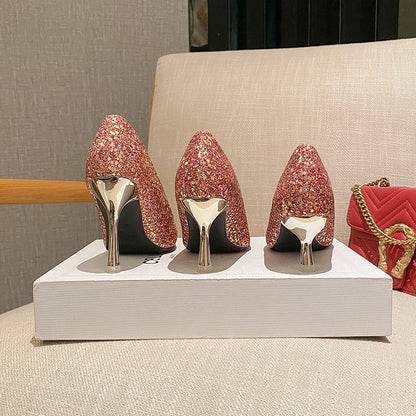 Three pairs of pink glittery high heel shoes with gold heels displayed on a white box on a beige chair