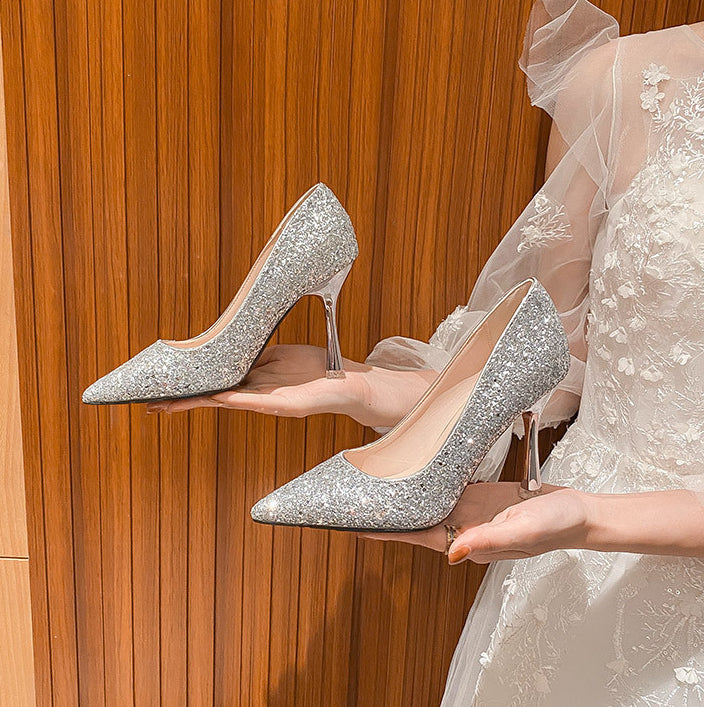Woman in white lace dress holding a pair of silver glitter pointed-toe high heel wedding shoes