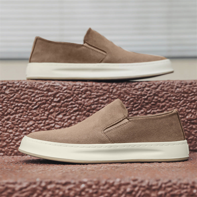 Brown suede slip-on casual shoes with white rubber soles displayed on textured brown steps