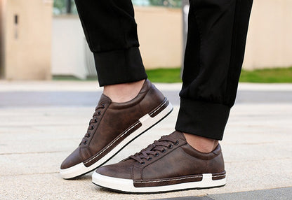 Men's brown leather casual sneakers with white rubber soles worn with black pants on pavement