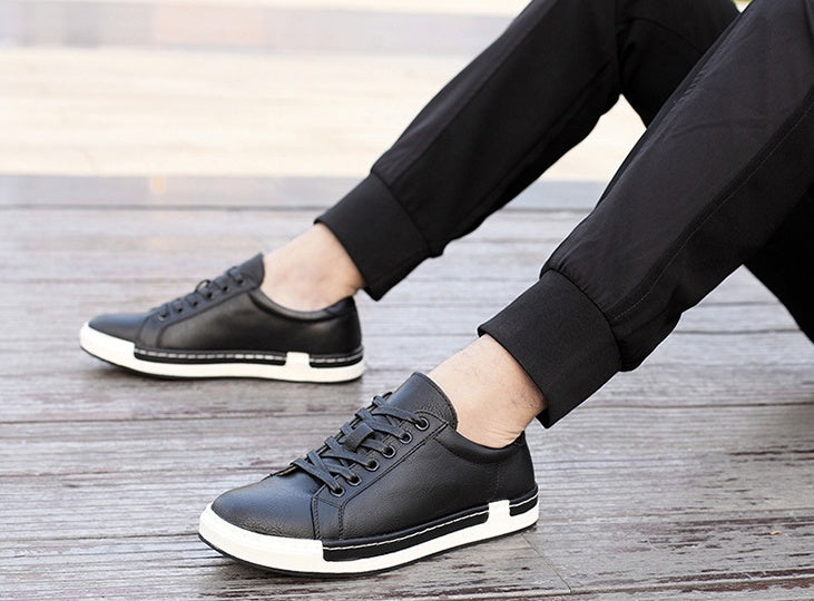Men's black leather sneakers with white rubber sole worn with black pants on wooden floor