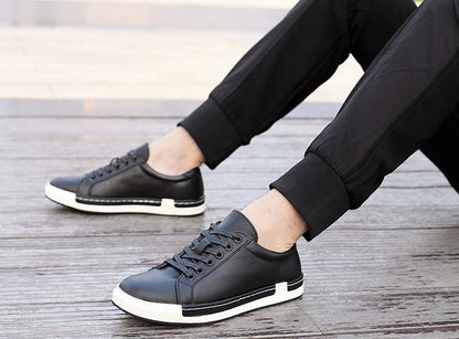 Men's black leather sneakers with white rubber sole worn with black pants on wooden floor