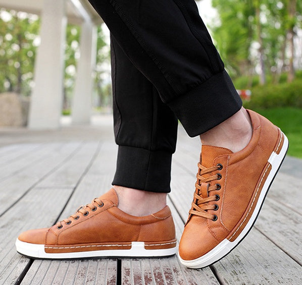 Men's brown leather casual sneakers with white rubber soles worn with black pants on wooden deck