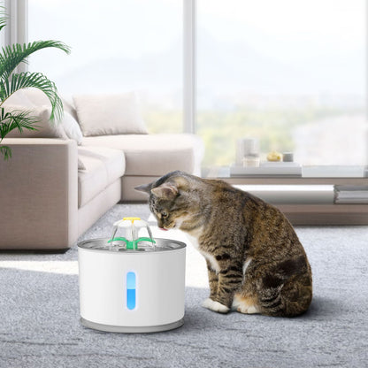 Gray tabby cat drinking from a white stainless steel USB-powered pet water fountain in a modern living room