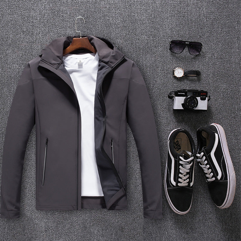 Gray waterproof mountaineering jacket with white T-shirt, black sneakers, sunglasses, watch, and camera on gray carpet