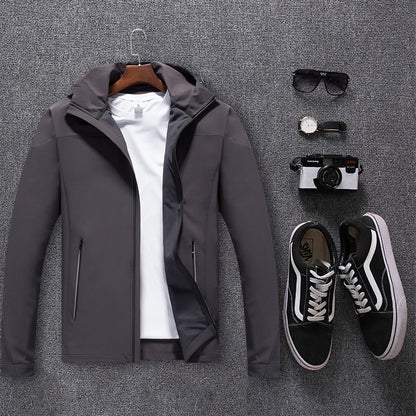 Gray waterproof mountaineering jacket with white T-shirt, black sneakers, sunglasses, watch, and camera on gray carpet