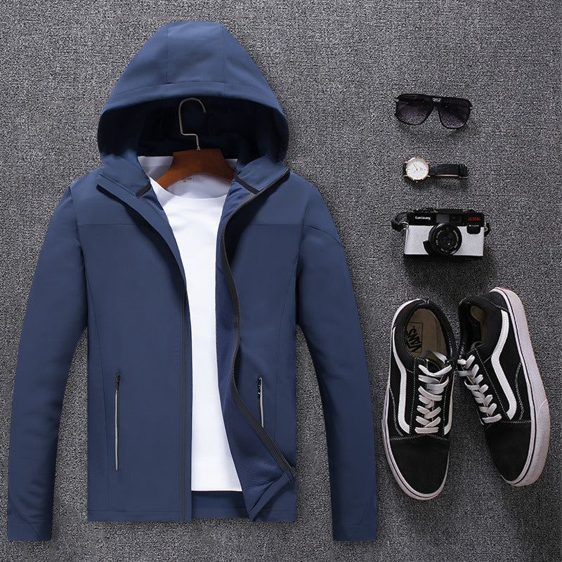 Blue waterproof mountaineering jacket with hood, white t-shirt, black sneakers, camera, sunglasses, and watch on gray background