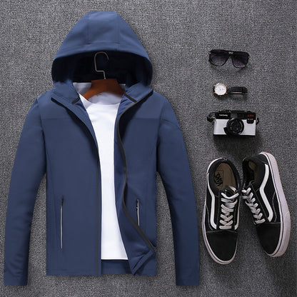 Blue waterproof mountaineering jacket with hood, white t-shirt, black sneakers, camera, sunglasses, and watch on gray background