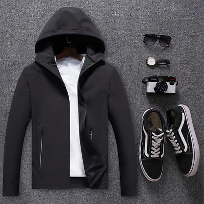 Black waterproof men's mountaineering jacket with hood, paired with white t-shirt, sunglasses, watch, camera, and black Vans sneakers on gray background