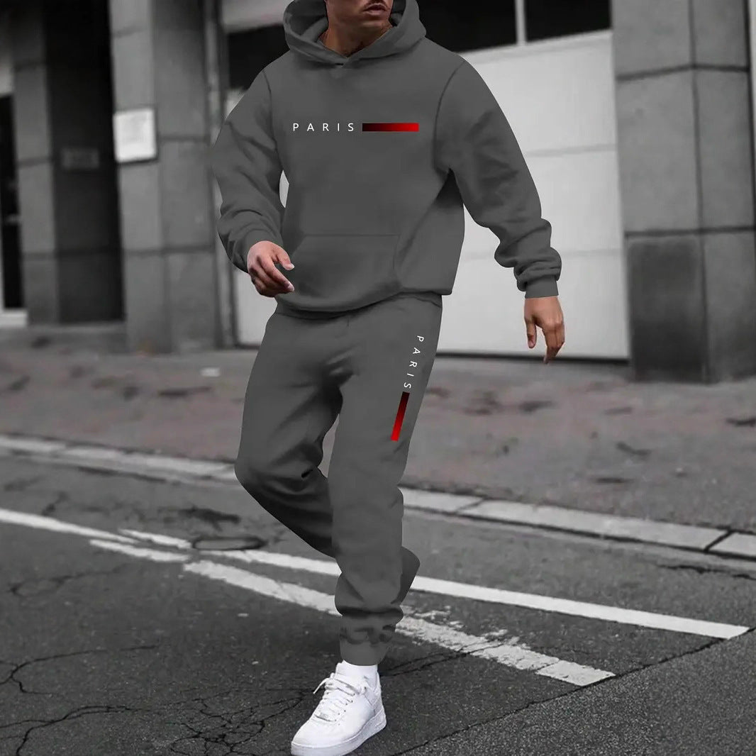 Man wearing gray hooded tracksuit set with Paris logo and white sneakers on urban street
