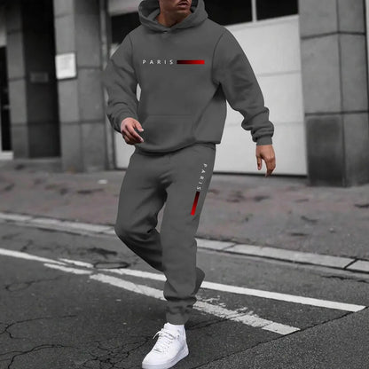 Man wearing gray hooded tracksuit set with Paris logo and white sneakers on urban street
