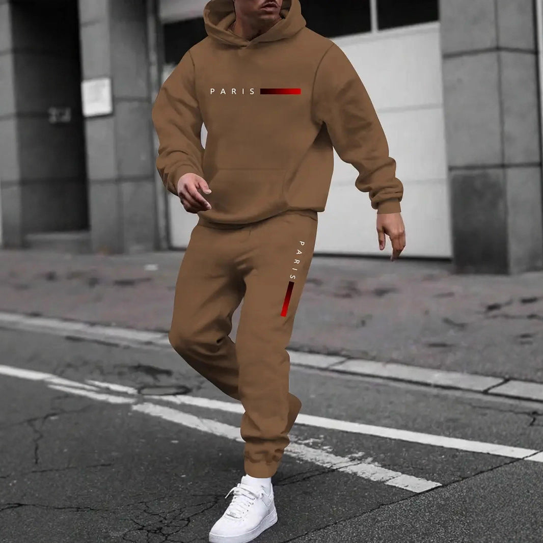 Man wearing brown hooded tracksuit with Paris text and red gradient bars, white sneakers on city street