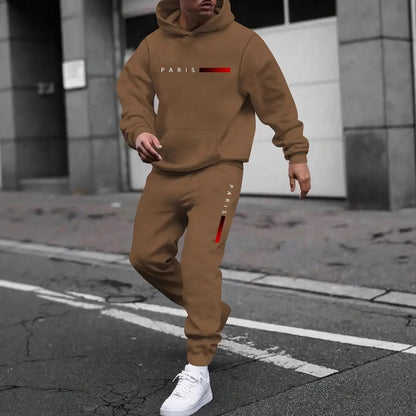 Man wearing brown hooded tracksuit with Paris text and red gradient bars, white sneakers on city street