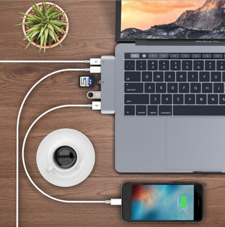 USB-C hub adapter connected to MacBook Pro with SD card, USB devices, and charging iPhone on wooden desk
