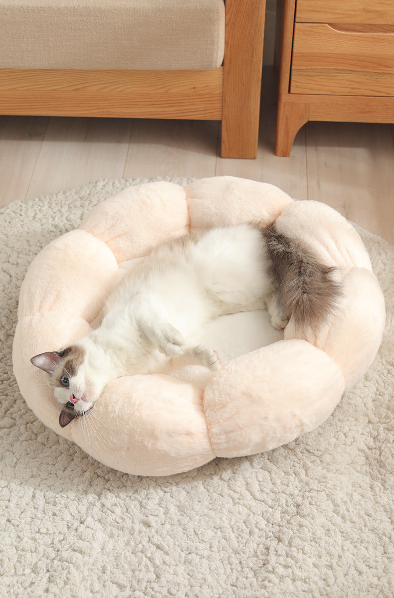 Fluffy white and gray cat lying comfortably in a plush beige flower-shaped pet bed on a textured rug