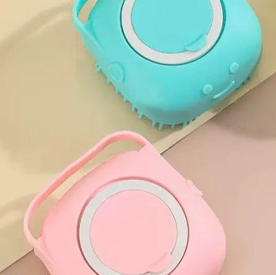 Blue and pink silicone dog bath brushes with soft bristles and shampoo dispenser handles on beige surface